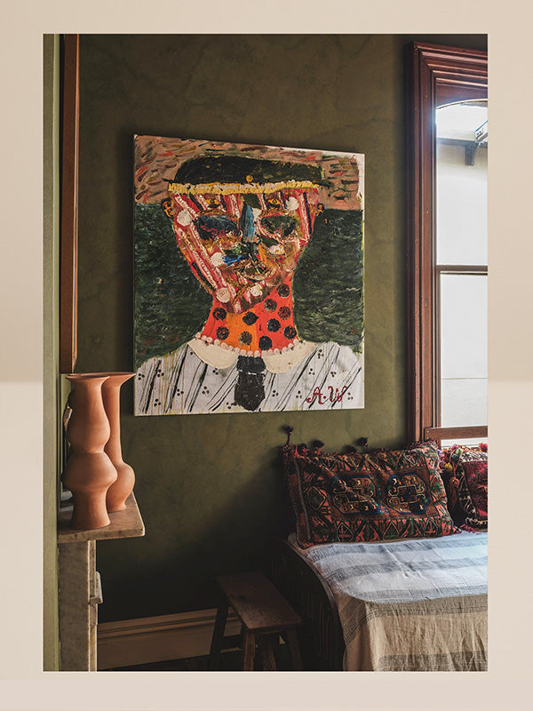 Artistic mosaic of a face on a wall in a room with a bench and vase.