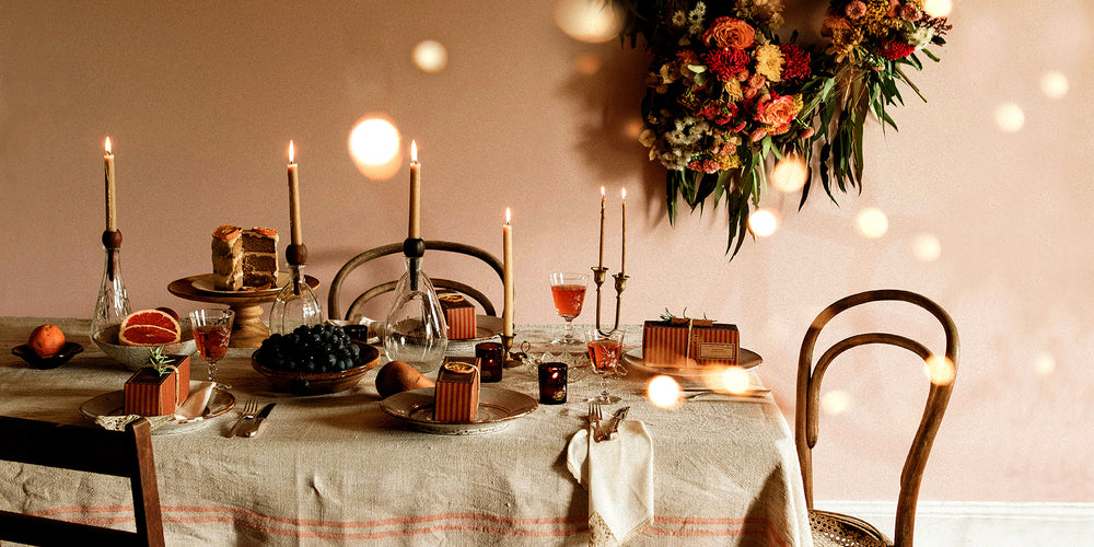 A christmas table setting adorned with beeswax candles and gifts. There is a large floral wreath hanging on a pink wall in a vintage home in country NSW Australia – Southern Wild Co
