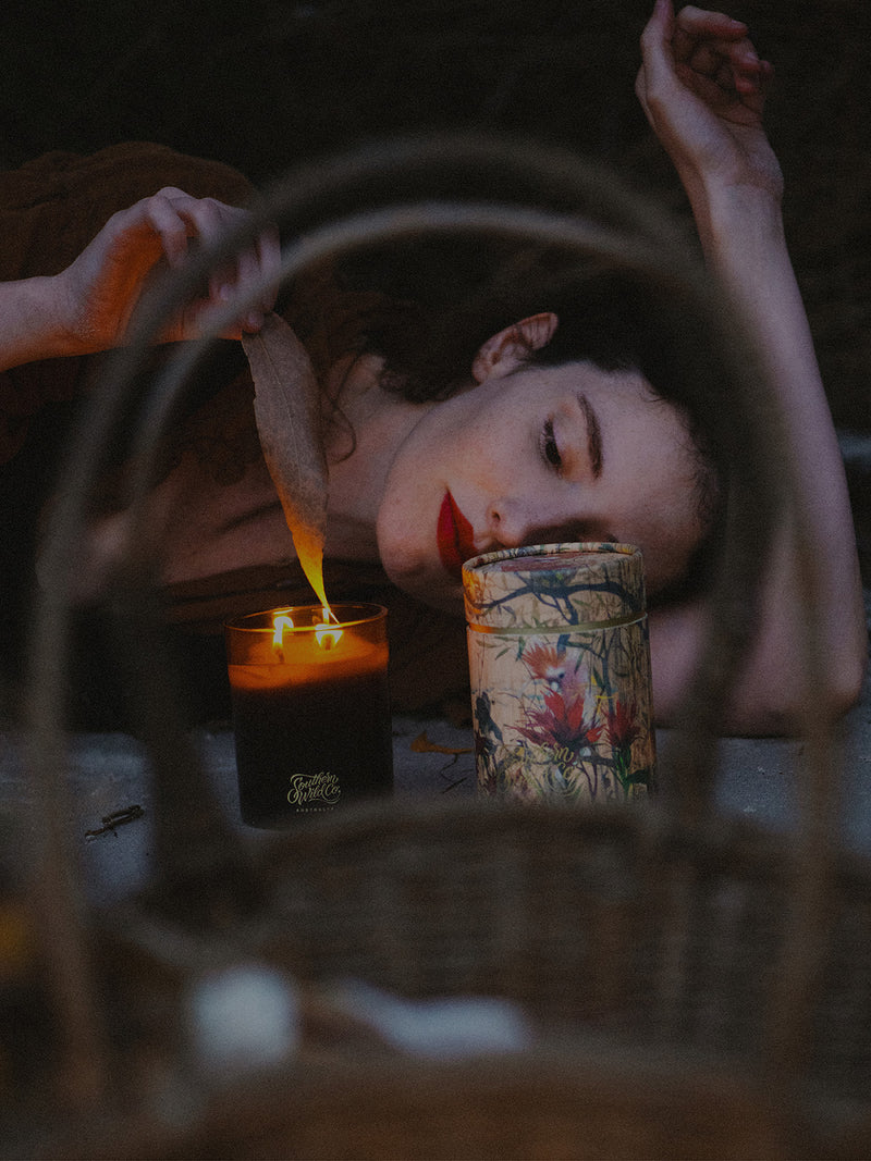 A dreamy twilight scene with Elle-May Watson lighting the Bush Magic candle, surrounded by nature, art, and the quiet enchantment of dusk.