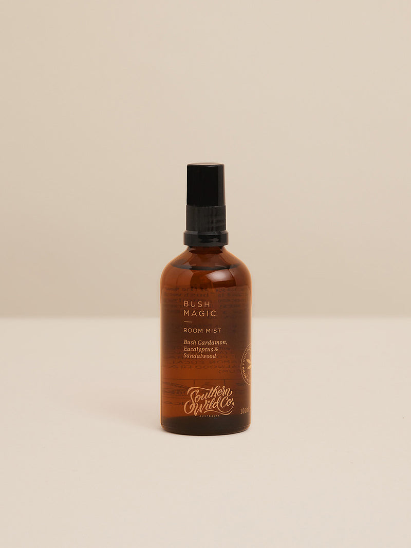 Studio product image of Bush Magic Room Mist in amber glass bottle, featuring scent notes of bush cardamom, eucalyptus and sandalwood against a neutral backdrop.