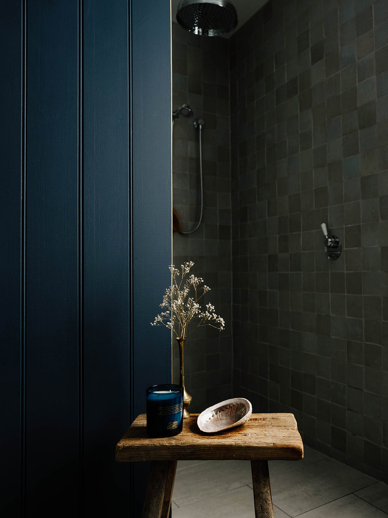 Ocean Isle candle placed beside a dried sprig and abalone shell on an old timber stool in a moody tiled bathroom—a ritual of sea-scented stillness.