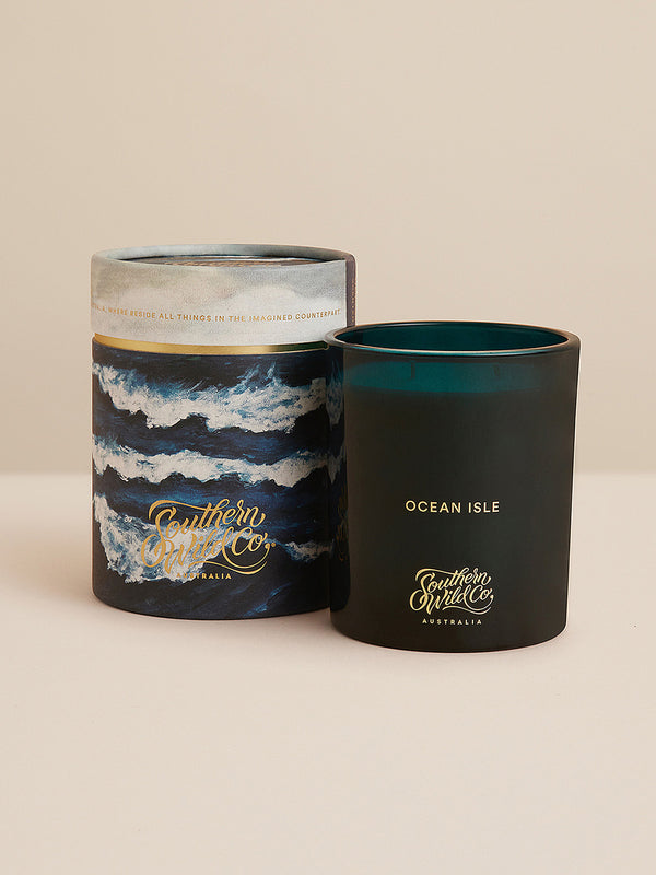 Ocean Isle candle with matching illustrated cylinder packaging, featuring crashing ocean waves and elegant Southern Wild Co gold foil branding.