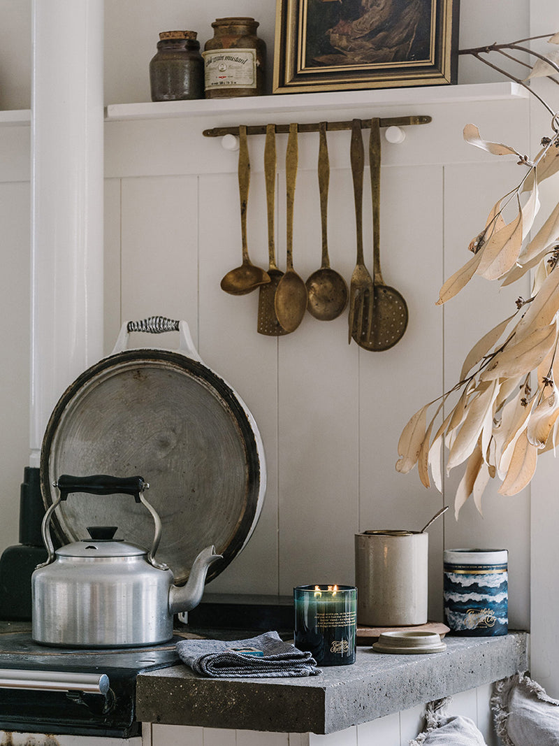 Ocean Isle candle flickering beside a vintage kettle and coastal-inspired tin in a rustic bush kitchen filled with character and charm.