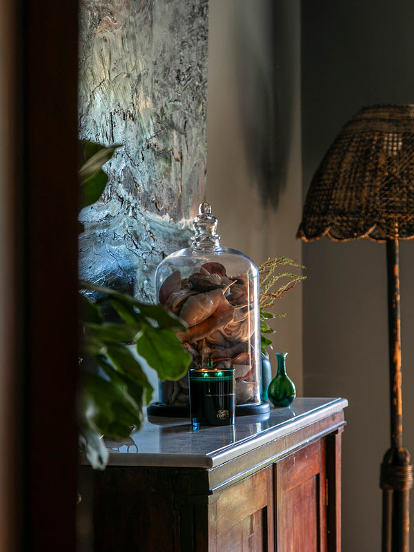 Ocean Isle candle glowing on a marble-topped cabinet beside a glass cloche filled with shells—bringing the coast inland with scent, texture, and memory.