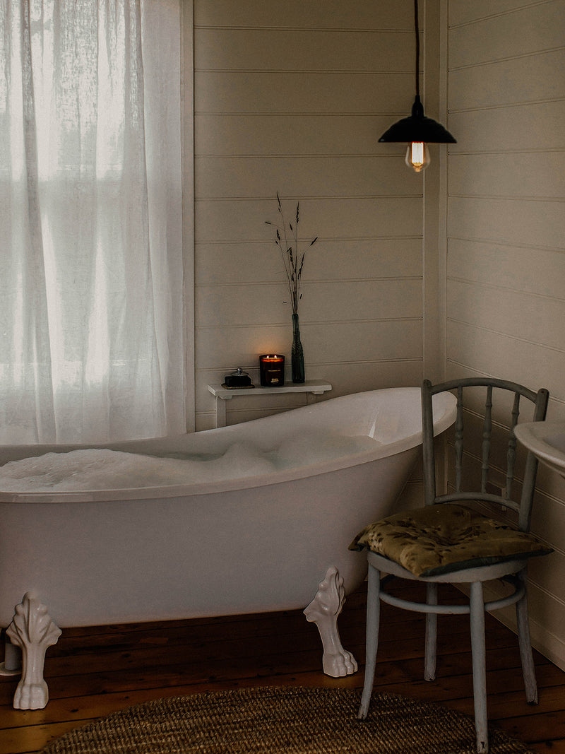 Lit Our Place candle by Southern Wild Co beside a clawfoot bath with linen curtains and vintage chair – Australian made candle for slow bathing and restful rituals.