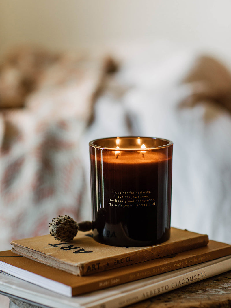 Our Place candle by Southern Wild Co placed on stacked art books with a dried seed pod – natural Australian candle with poetic inscription, perfect for bedroom styling and quiet reflection.