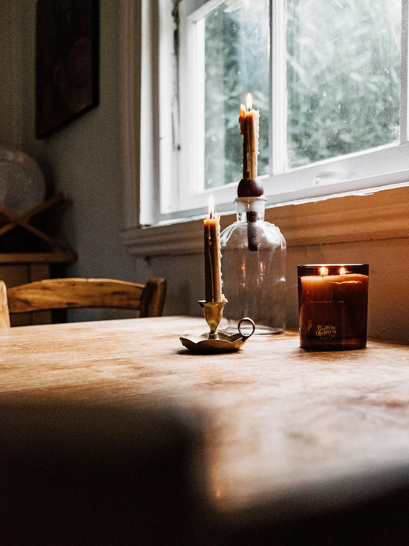 Our Place candle by Southern Wild Co glowing on a rustic kitchen table beside beeswax tapers and vintage glass – artisan Australian candle for slow moments and nostalgic interiors.