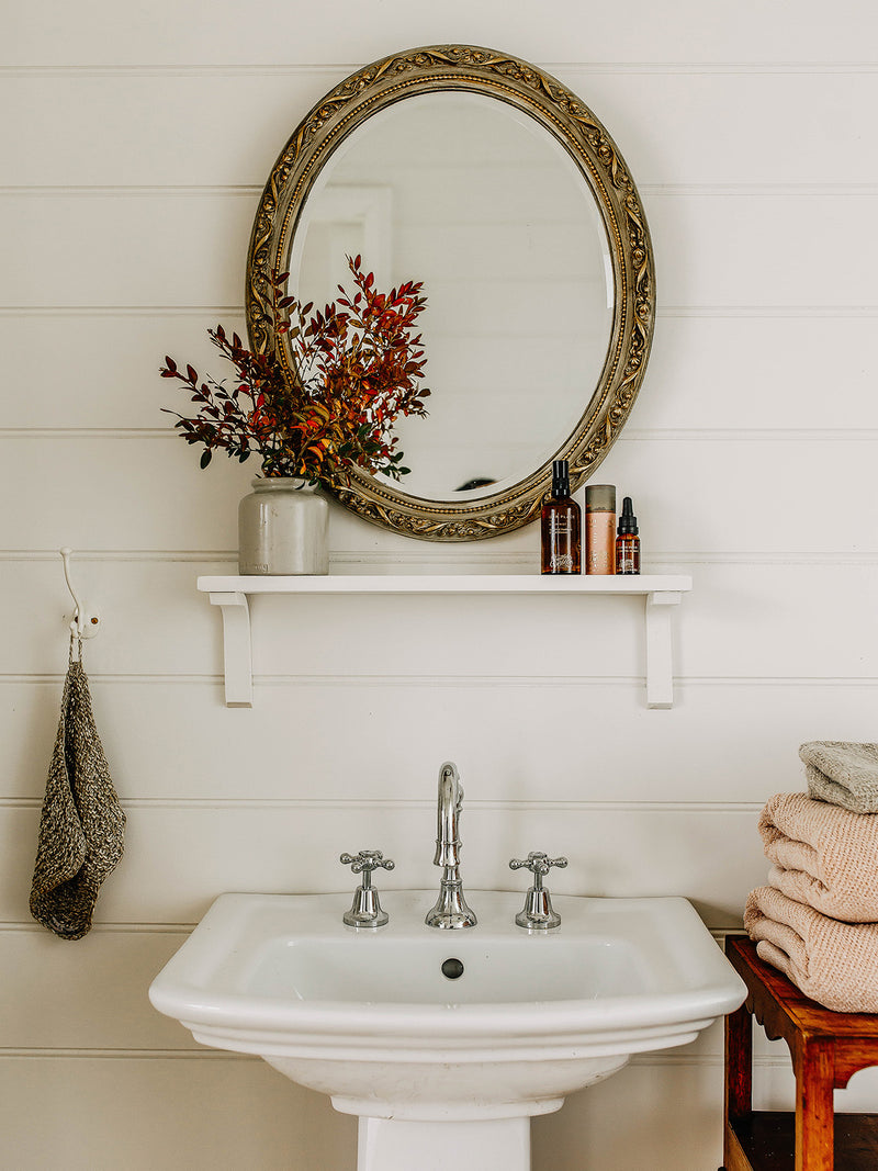 Our Place Room Mist by Southern Wild Co styled in a country bathroom with a vintage mirror, botanical arrangement, and soft folded towels – Australian made room spray for calming, naturally scented spaces.