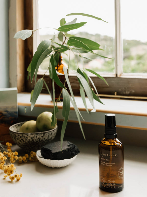 Our Place Room Mist by Southern Wild Co styled near a windowsill with gum leaves, lemons, and soap – artisanal Australian room spray inspired by the scent of bushland and summer air.