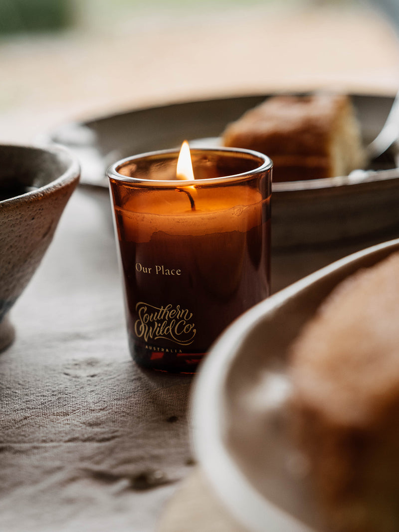 Southern Wild Co’s Our Place votive candle glowing during afternoon tea beside rustic ceramic plates and cake – Australian soy candle perfect for table settings and daily rituals.