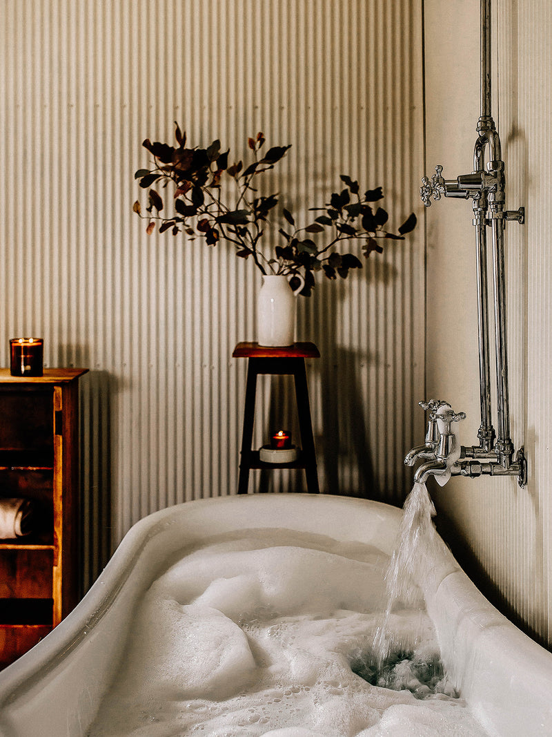 Our Place votive candle by Southern Wild Co beside a running clawfoot bath in a corrugated iron bathroom – artisan soy candle for slow bathing and mindful self-care.