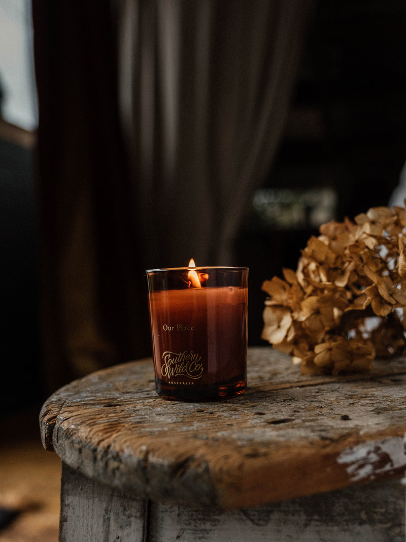 Lit Our Place votive candle by Southern Wild Co on a weathered timber stool with dried hydrangeas – handcrafted Australian candle evoking warmth and nostalgia.