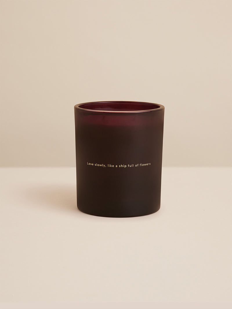 Close-up of Sirens candle in deep plum glass with gold-foiled quote: “Love slowly, like a ship full of flowers” – a signature piece by Southern Wild Co.