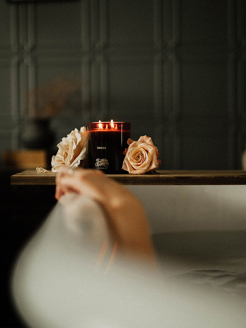 Southern Wild Co Sirens candle beside a warm bath and soft peach roses – a ritual of scent, warmth and stillness.