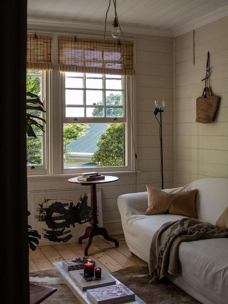 Sirens candle styled in a sunlit living room with layered books, cowhide rug and soft linen textures – a slow living scene with scent and story.