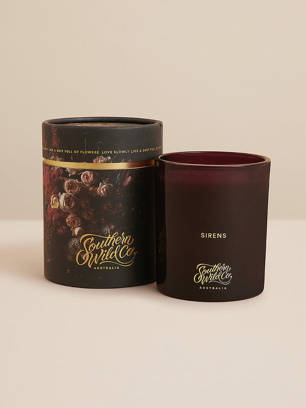 Southern Wild Co’s Sirens candle glowing against dark moody tones, softened with dried branches and blush roses – evocative and romantic.