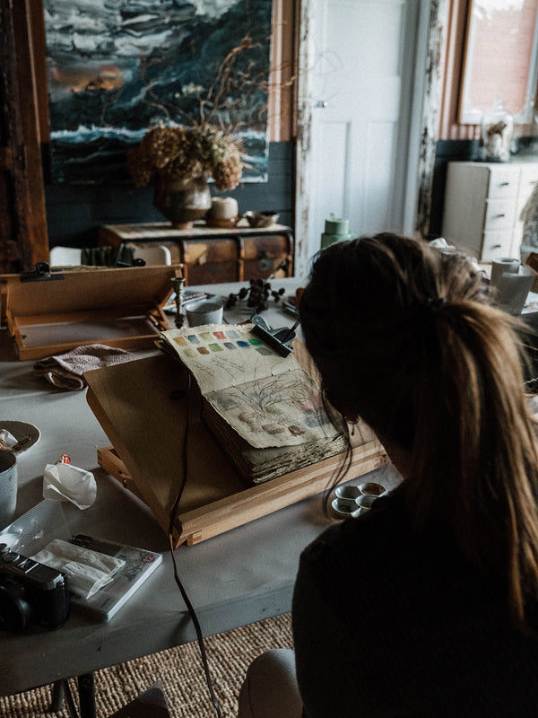 Person working at a desk with art supplies and a Southern Wild Co Sketchbook in a studio setting