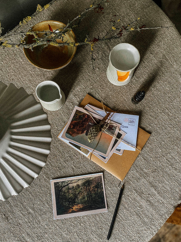 Tabletop scene with Southern Wild co postcards, essential oil and burner on a natural linen cloth.