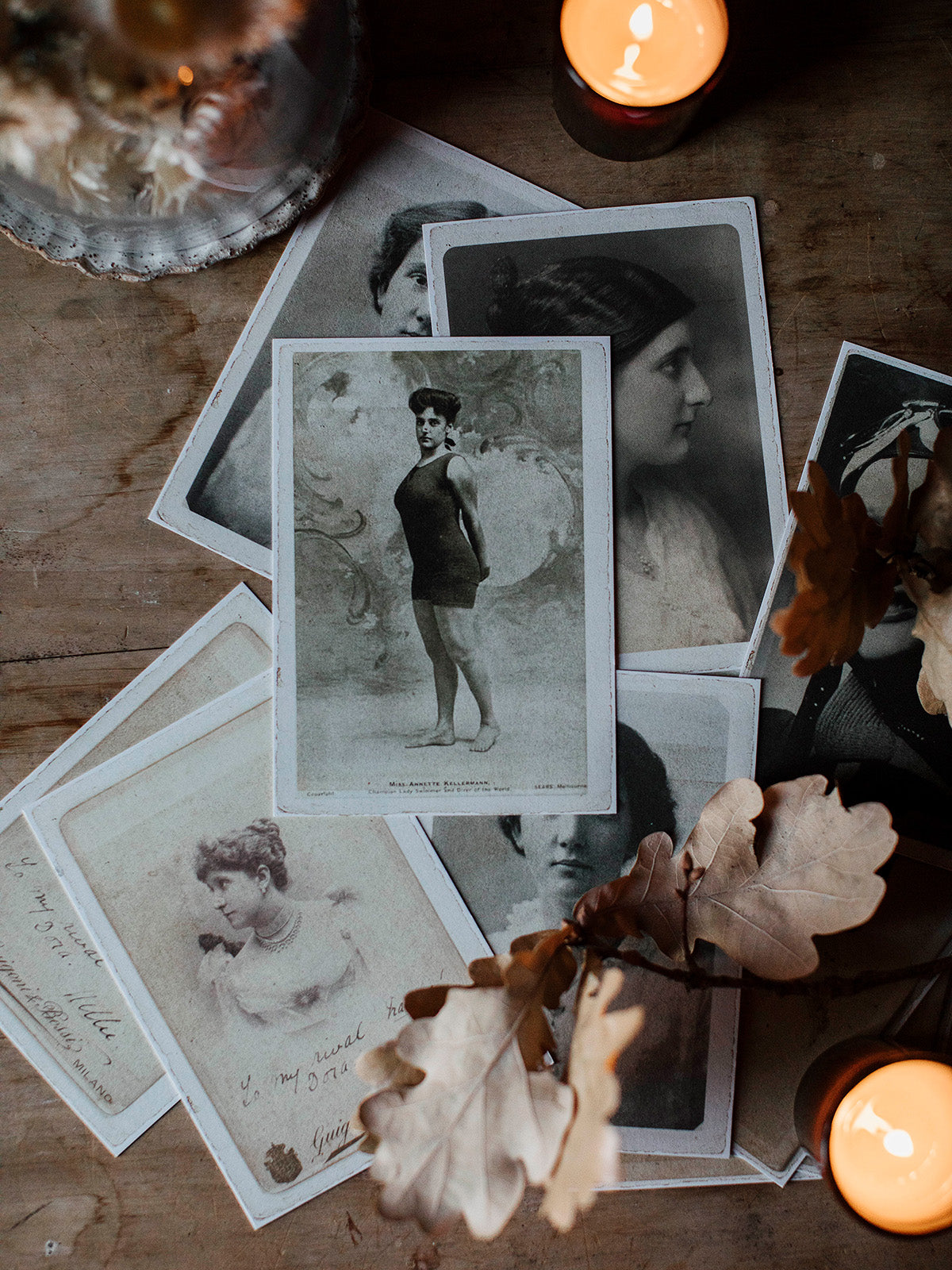 Southern Wild Co Vintage photographs and cards on a wooden surface with candles and leaves.