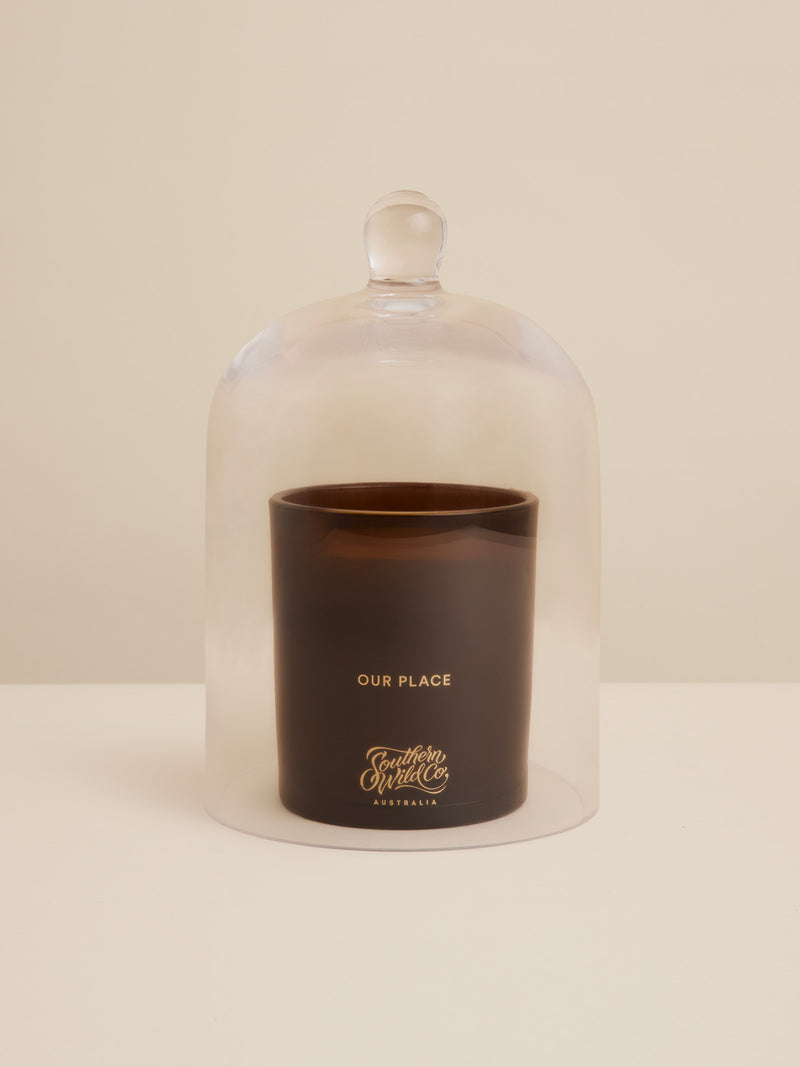 Southern Wild Co’s “Our Place” candle encased in a clear glass cloche — a still-life of scent, light, and slow-living refinement.