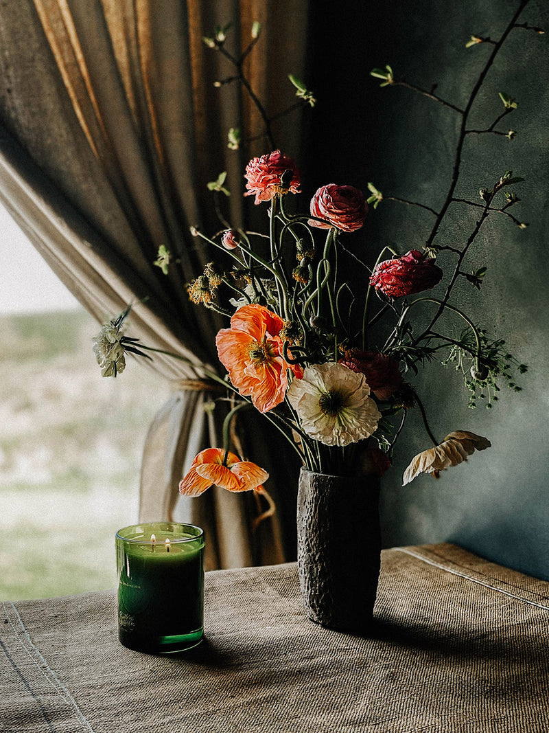 Southern Wild Co’s Hidden Vale candle lit beside a vase of poppies and wild garden flowers – artisan soy candle styled in a moody, sunlit interior for seasonal home rituals.