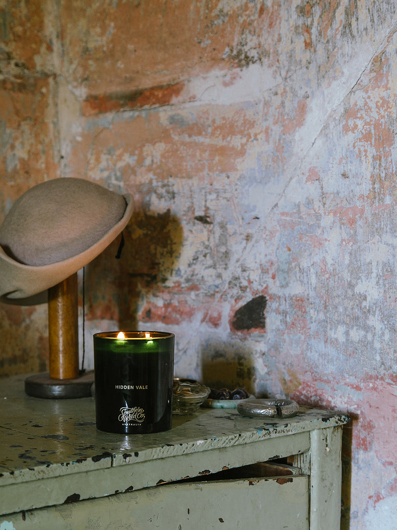 Hidden Vale candle by Southern Wild Co glowing on a rustic green cabinet against a weathered plaster wall – Australian made scented candle for vintage interiors and nostalgic rituals.
