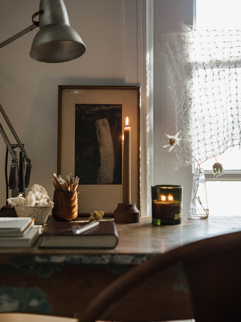 Lit Hidden Vale candle by Southern Wild Co on a vintage writing desk with books, art, and soft natural light – handmade Australian candle for creative spaces and quiet moments.