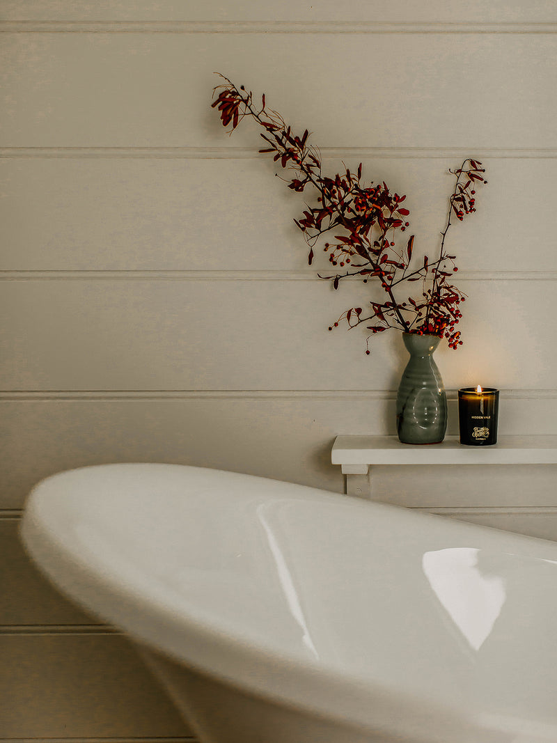 Southern Wild Co’s Hidden Vale candle styled in a minimalist bathroom with a freestanding tub and native branches – luxury Australian candle for relaxing bath rituals and self-care.