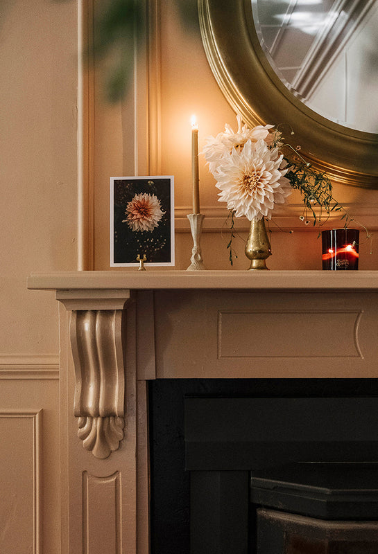 Decorative mantelpiece with candles, flowers, and a framed picture against a beige wall.