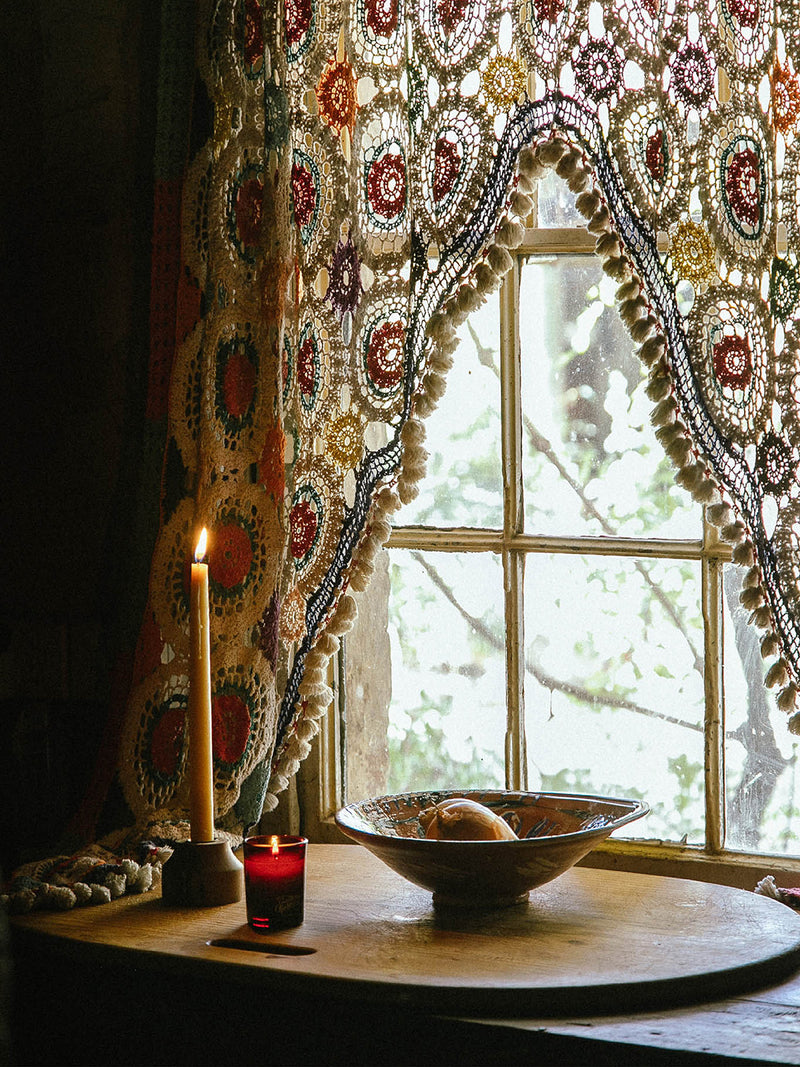 Sirens votive candle glowing in a rustic kitchen window nook with a tall beeswax taper and crochet lace curtain – Southern Wild Co’s slow ritual of scent and story.