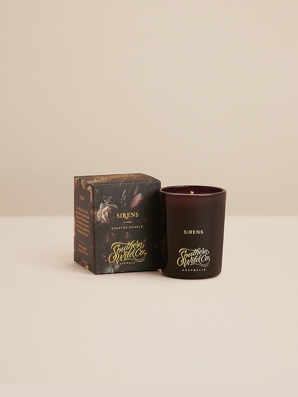 Sirens votive candle and illustrated floral box on a neutral backdrop – Southern Wild Co’s rose-led scent in a deep plum glass, small in size, rich in mood.