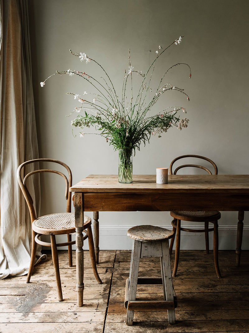 Rustic dining table with chairs and a vase of flowers and Southern Wild Co candle.