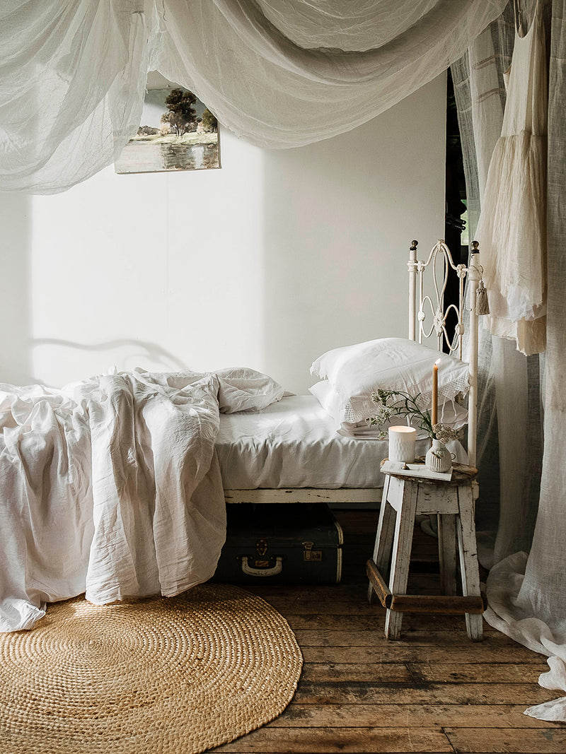 Cozy bedroom with canopy bed, wooden floor, and draped curtains, and Southern Wild Co candle.