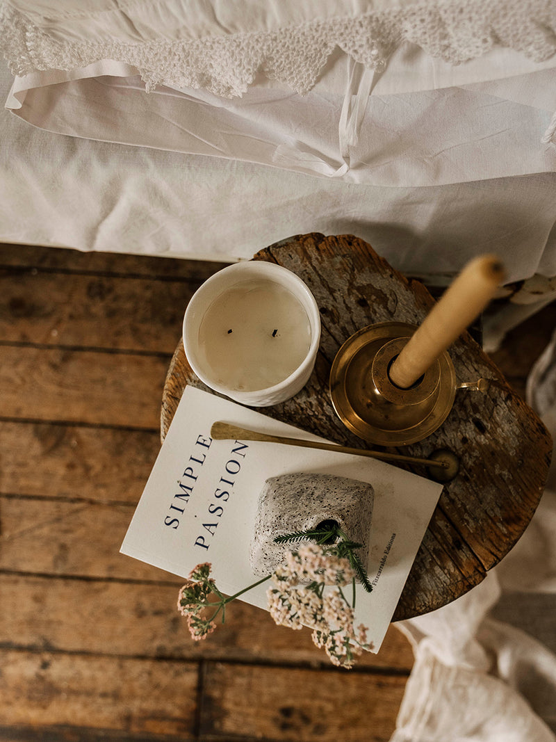 Candle, book titled 'Simple Passion', and small bouquet of flowers on a wooden surface.