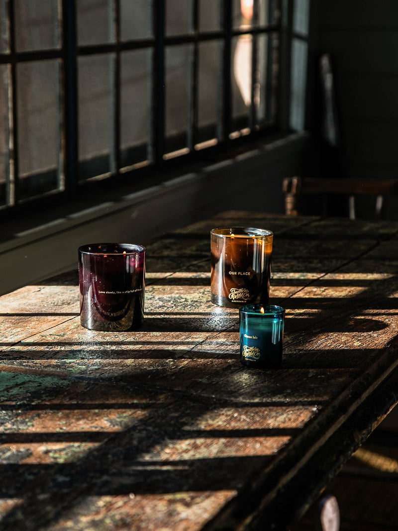 Three candles on a wooden surface with sunlight filtering through a window.