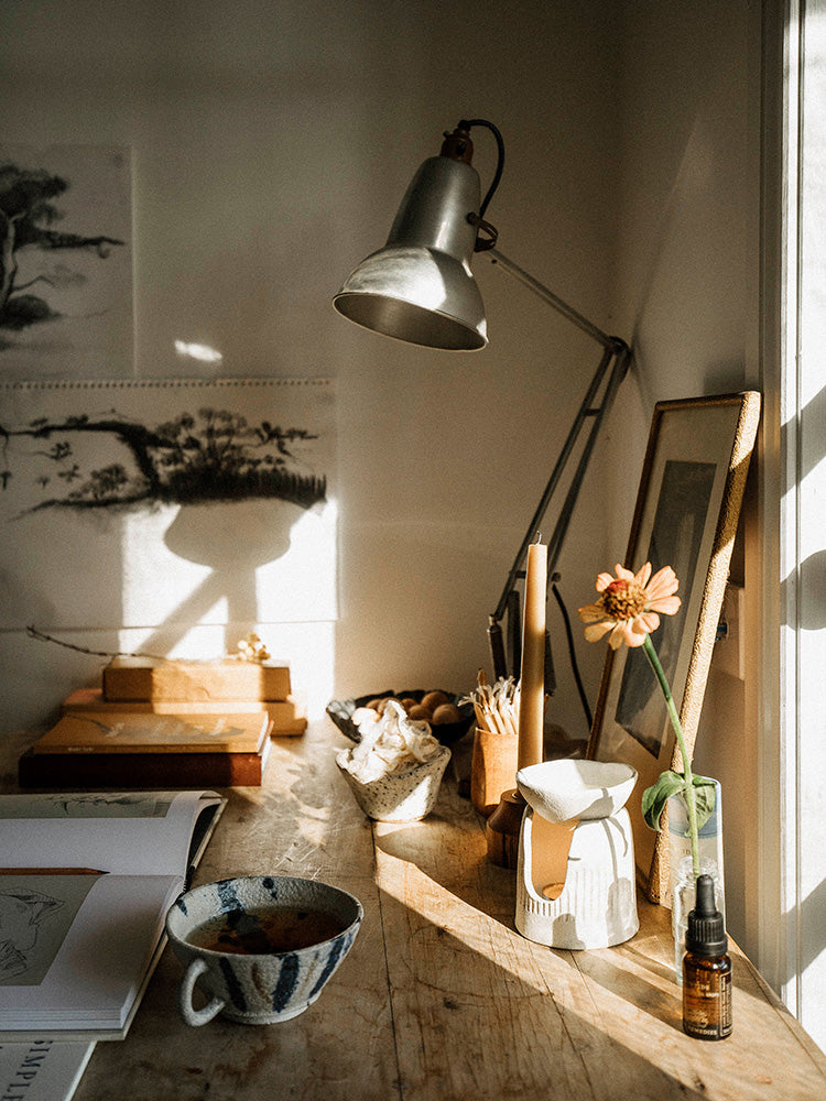 Candle, flower and essential oil burner on a wooden table with a window in the background