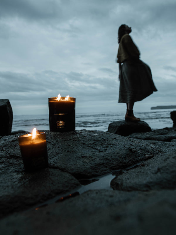 Southern Sky candles flicker on ocean-washed rock as dusk falls, a lone figure gazing skyward—an ode to the vast Australian sky and moments of quiet reflection by the sea.