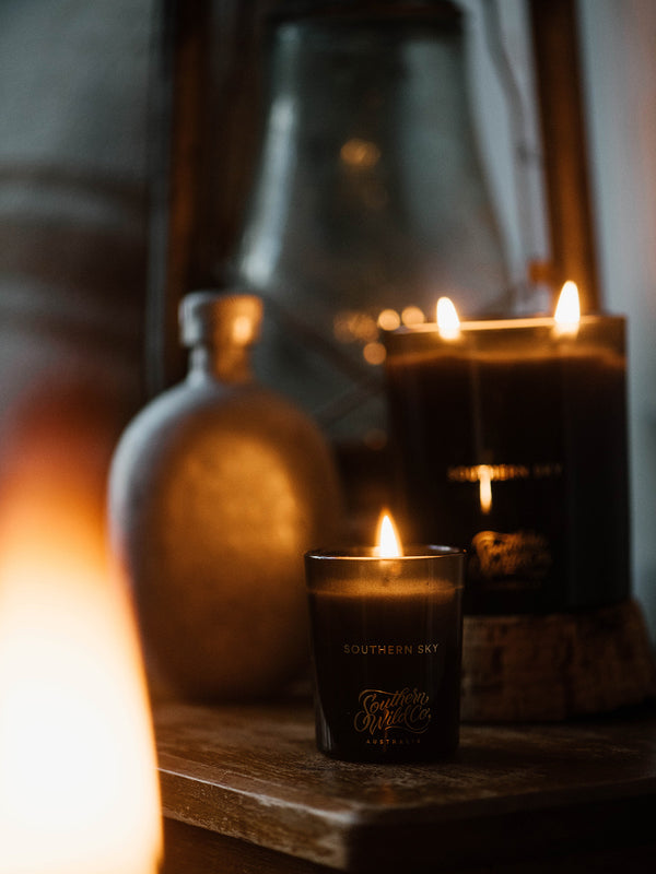 Southern Sky votive and large candle flickering beside earthenware and wood—an Australian candle duo that brings warmth and starlit stillness into your space.