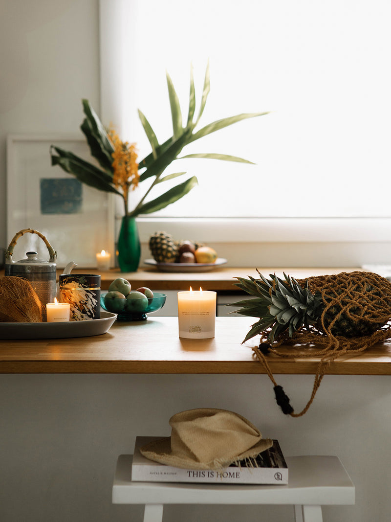 Bright and breezy kitchen moment with the Sunshine candle lit beside tropical fruit, sea treasures, and warm morning light streaming through the window.
