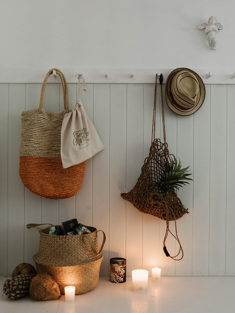 Entryway styled with coastal textures — woven baskets, shells, and the glowing Sunshine candle creating a welcoming, beachside calm.