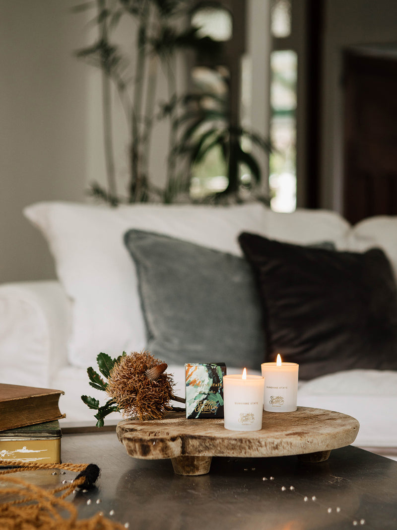 Sunshine votive candle styled with Australian wildflowers and painterly packaging, creating a warm welcome on a rustic timber coffee table.