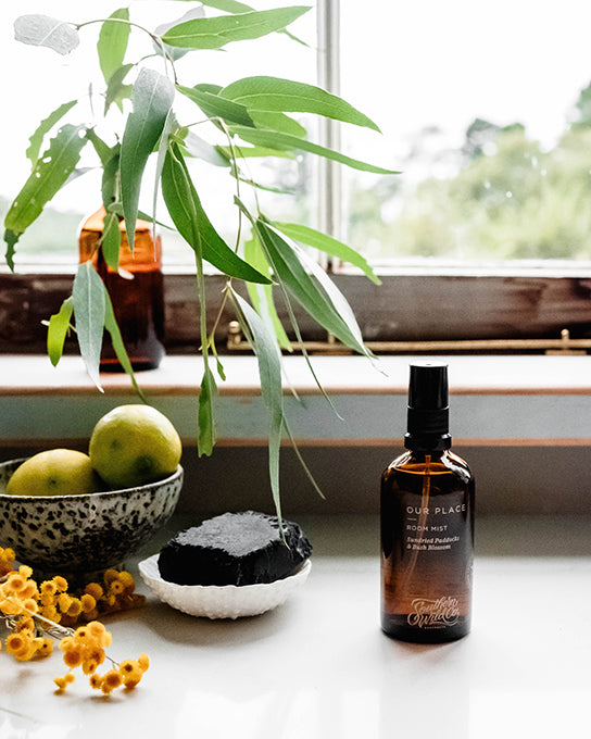 Southern Wild Co Room Mist in best-selling fragrance, Our Place. The room mist is on a beautiful kitchen bench in the style of a deVol kitchen. There is a stem of fresh eucalyptus in an amber bottle on the window sill and a bowl of lemons. 